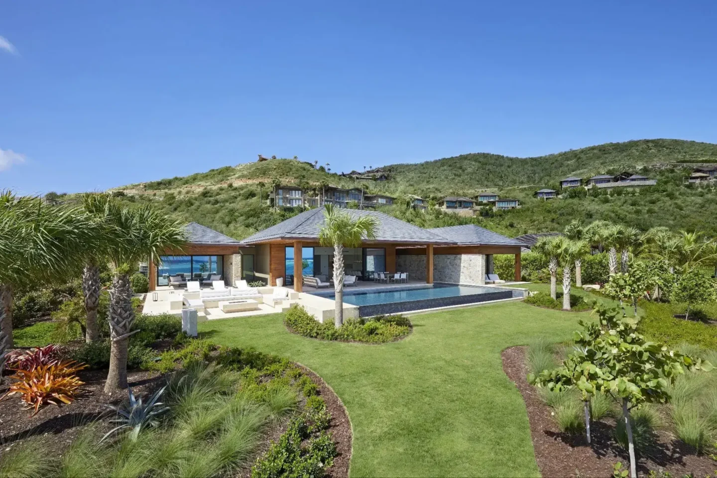 Lush palm trees and colorful tropical flowers frame a beach house, embodying a serene and inviting island vibe.