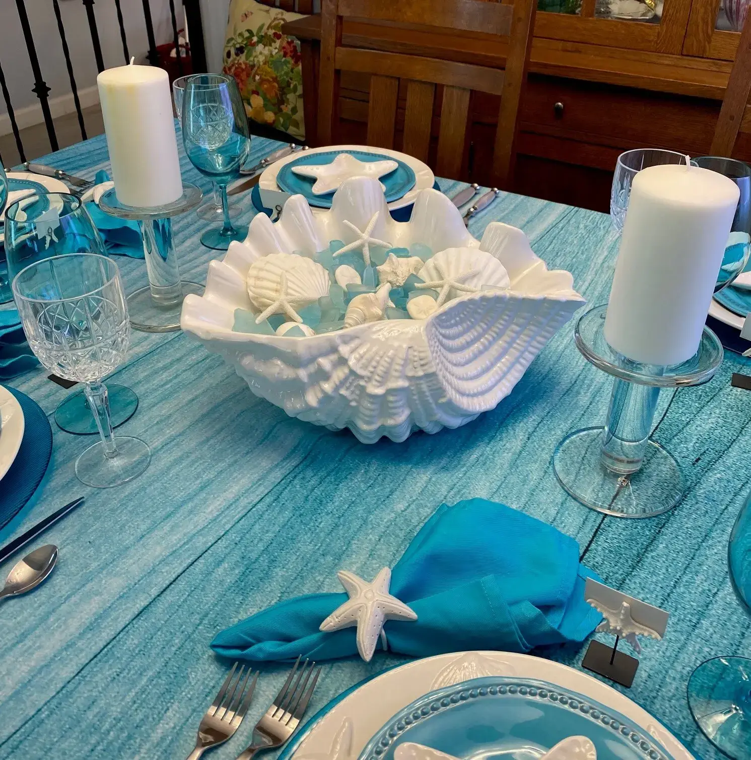 Beach-themed table setting featuring decorated wine glasses and mason jars and seashells for a coastal charm