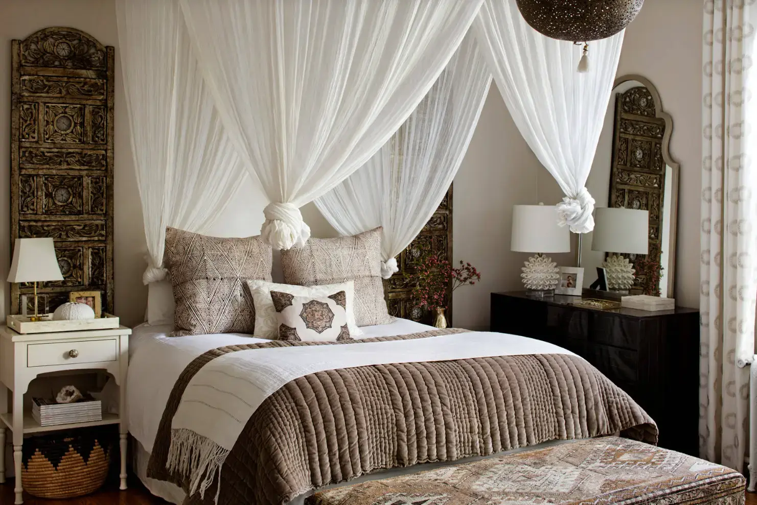 A bed draped with a sheer canopy and adorned with white and pastel bedding