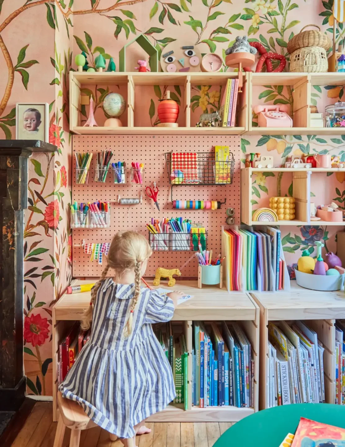 A young girl is engaged at her table, her back to us, with a pegboard wall behind her for doll storage and organization
